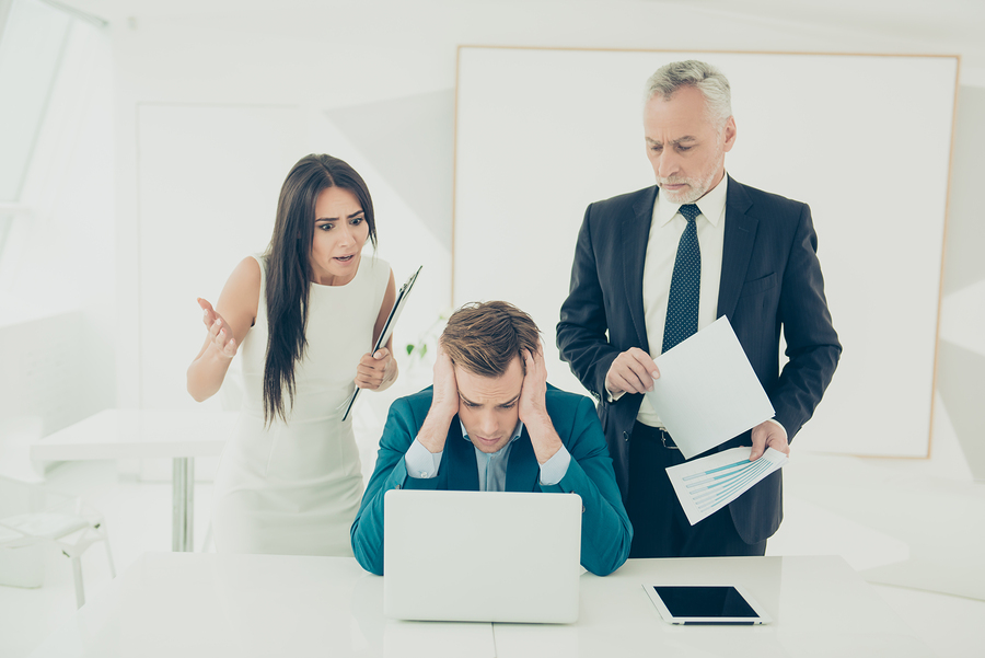 man looking at laptop upset while man and woman stand over him surprised