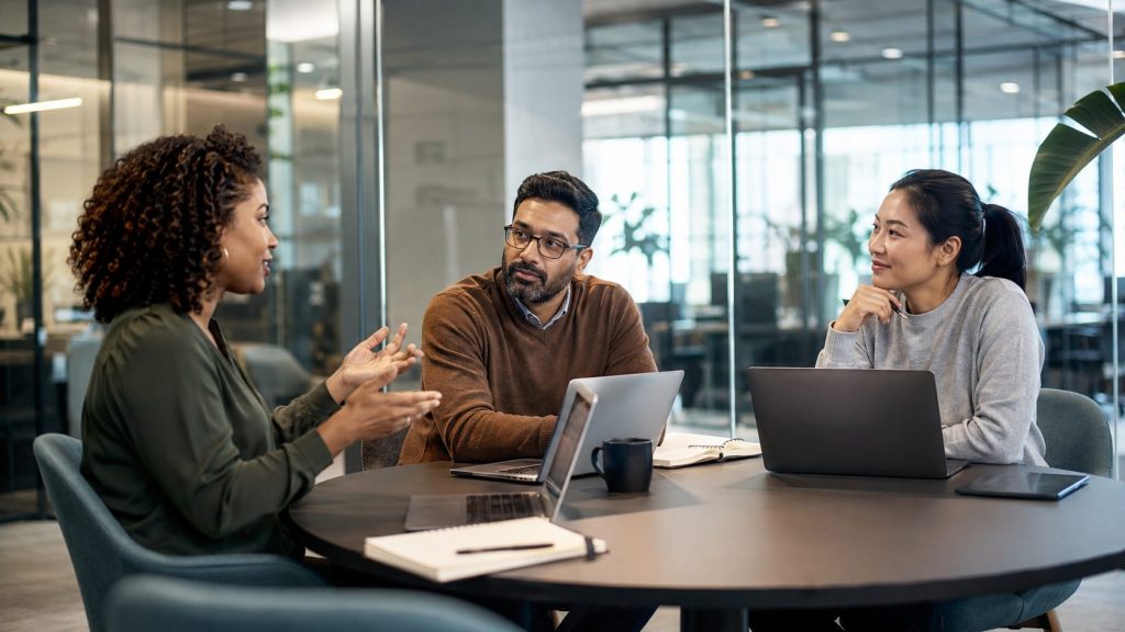 A diverse team of three professionals collaborating around a round conference table